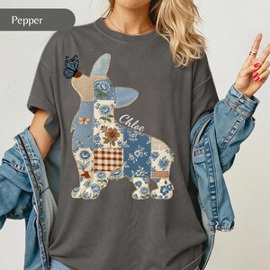 Può includere: Una t-shirt a maniche corte grigio antracite con una grande grafica raffigurante la sagoma di un cane riempita con un motivo patchwork blu e marrone di fiori, quadri e una farfalla. Il nome Chloe è stampato in corsivo bianco accanto alla grafica.