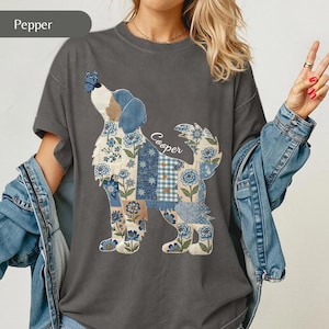 Puede incluir: Una camiseta gris pimienta de manga corta con el gráfico de un perro compuesto por parches de estilo patchwork con motivos florales y cuadros en azul y blanco. Una mariposa azul descansa sobre la nariz del perro y el nombre Cooper está en blanco.