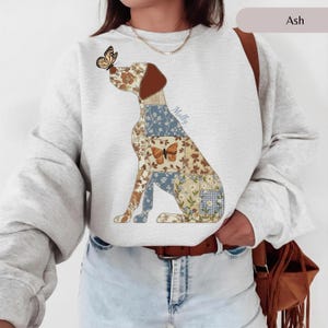 May include: An ash gray crewneck sweatshirt featuring a large graphic of a dog composed of various floral and checkered patchwork patterns in shades of blue, brown, and cream. A butterfly rests on the dog's nose, and the name Molly is printed.