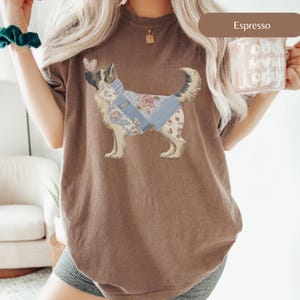 Puede incluir: Camiseta color espresso con un gráfico de un perro con un diseño floral y patchwork. El perro tiene una mariposa en la nariz. La camiseta es de un estilo cómodo e informal.