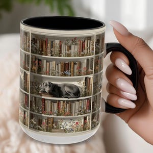 May include: A ceramic mug with a black handle and interior, featuring a wrap-around print of white bookshelves filled with various books and colorful wildflowers. A grey dog is lying down on one of the shelves among the books.
