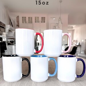 May include: Six white ceramic mugs with colored handles and interior rims. The handles are red, pink, black, blue, and navy. The mugs are labeled "15oz".