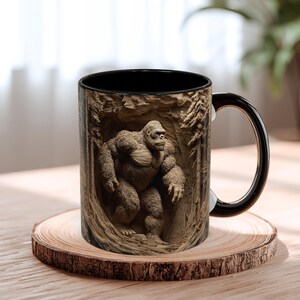 May include: A black and brown coffee mug featuring a detailed relief of a gorilla in a forest setting. The mug has a black interior and handle, and is set on a wooden coaster. The gorilla is depicted in a realistic style.