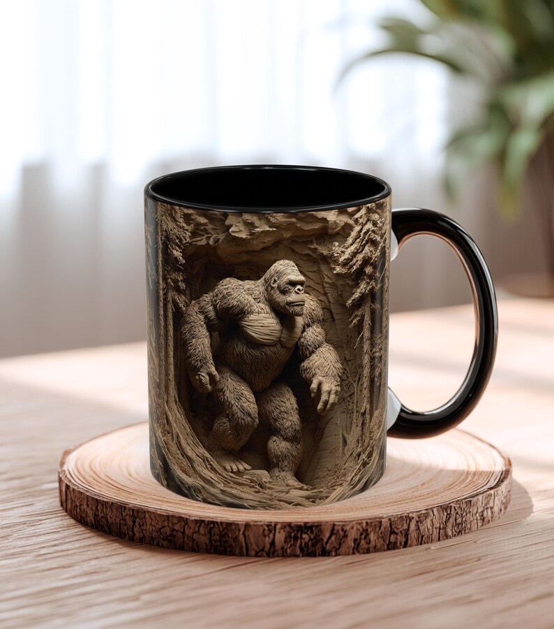 May include: A black and brown coffee mug featuring a detailed relief of a gorilla in a forest setting. The mug has a black interior and handle, and is set on a wooden coaster. The gorilla is depicted in a realistic style.