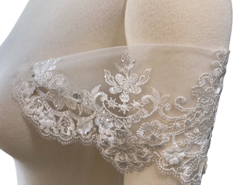 May include: An off-the-shoulder sleeve accessory made of sheer white tulle fabric. The sleeve features intricate white floral embroidery, scalloped edges, and small three-dimensional fabric flower appliqués accented with subtle silver sequins.