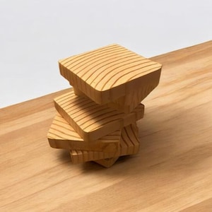 May include: A stack of four wooden blocks, each with a unique shape and grain pattern. The blocks are made of light brown wood and are stacked on top of each other.