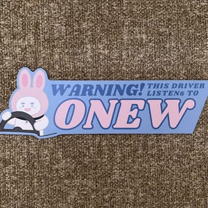 May include: A light blue sticker with the text "WARNING! THIS DRIVER LISTENS TO ONEW" in pink and white. The sticker features a cartoon character in a bunny hat driving a car.