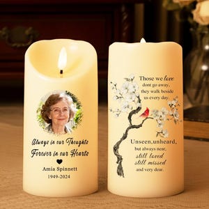 May include: Two ivory-coloured LED candles with a flickering flame. One candle features a photo of a woman and the text "Always in our Thoughts, Forever in our Hearts." The other candle has a floral design and the text "Those we love don't go away."