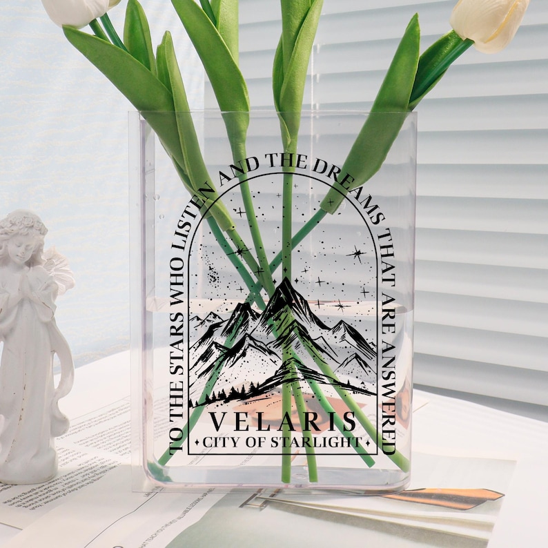 Pu&ograve; includere: Un vaso di vetro trasparente con un design grafico nero che presenta una catena montuosa, stelle e il testo "To the stars who listen and the dreams that are answered. Velaris. City of Starlight."