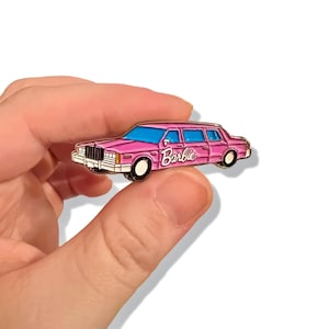 May include: Pink Barbie car enamel pin. The car is a pink limousine with the word "Barbie" written on the side.
