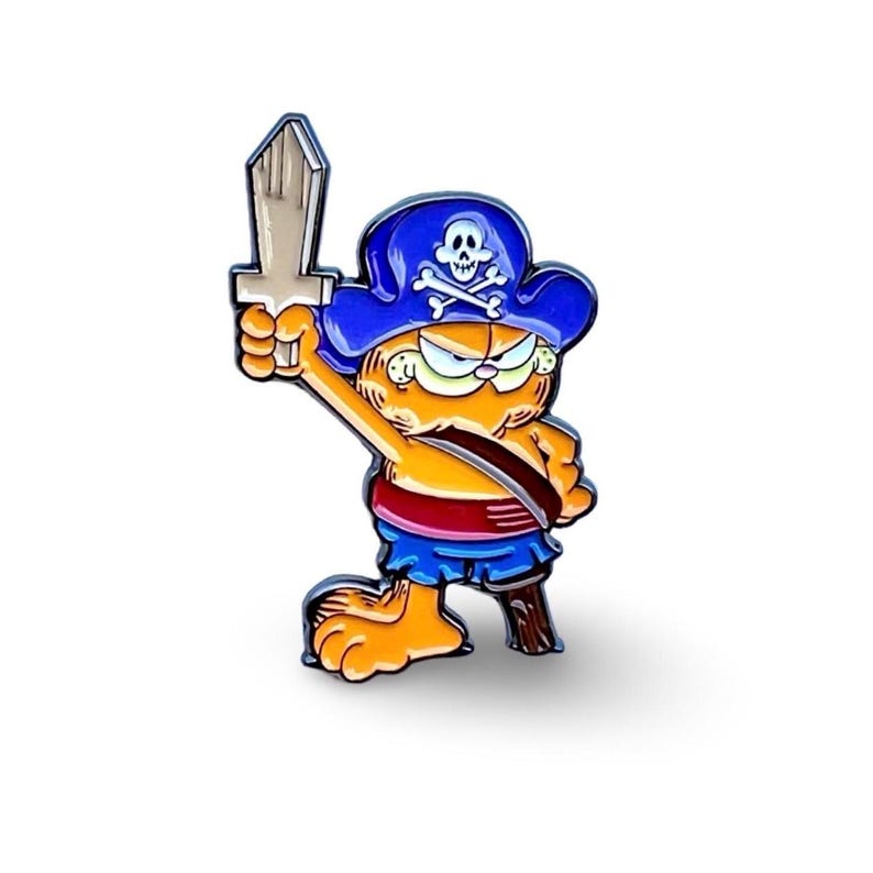 May include: An orange cartoon cat wearing a blue pirate hat with a skull and crossbones design, holding a wooden sword in its right paw. The cat is wearing a red and blue pirate outfit.
