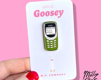 Könnte beinhalten: Ein grüner Nokia-Telefon-Emaille-Pin mit dem Text "I'm in a boyband" auf einer weißen Karte. Die Karte trägt den Text "Pins by Goosey" in Rosa und eine Gänse-Illustration. Der Pin wird vor einem rosa Hintergrund gehalten.