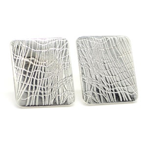 May include: A pair of silver square earrings with a textured, woven design.