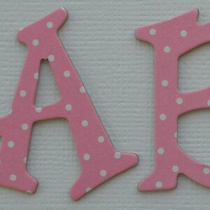 May include: Pink wooden letters spelling "ABC" with white polka dots and a pink flower with white polka dots and a yellow center.