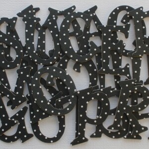 May include: Black and white polka dot letters, cut from paper, in a variety of sizes and styles. The letters are arranged in a random order.