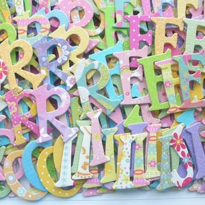 May include: A large collection of colorful wooden letters with glitter and floral patterns. The letters are in various shades of pink, blue, green, and yellow.
