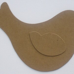 May include: A brown paper bird cutout with a smaller brown paper cutout inside, resembling a wing.