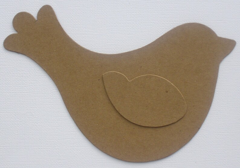 May include: A brown paper bird cutout with a smaller brown paper cutout inside, resembling a wing.