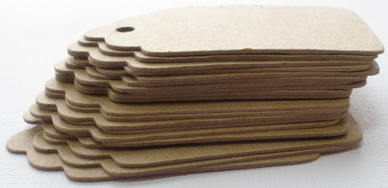 May include: A stack of brown paper gift tags with scalloped edges. The tags have a hole punched in the top for string or ribbon.