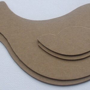 May include: Three layered wooden bird shapes, cut out in the shape of a bird with a heart in the center. The bird shapes are brown and are stacked on top of each other.