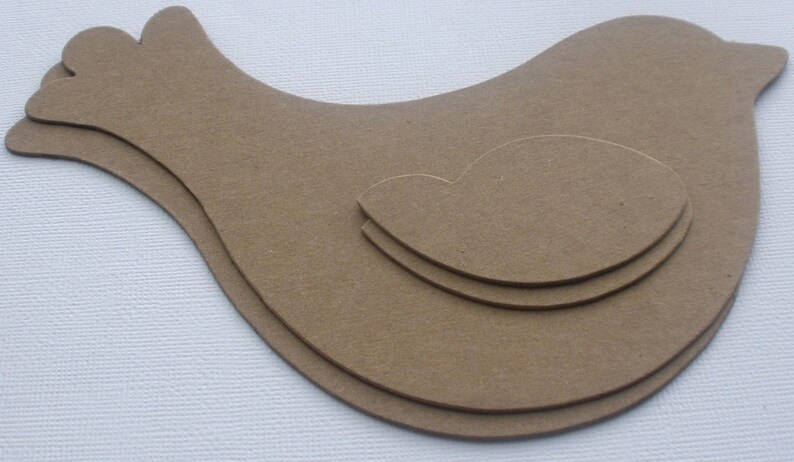 May include: Three layered wooden bird shapes, cut out in the shape of a bird with a heart in the center. The bird shapes are brown and are stacked on top of each other.