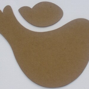 May include: A brown paper cutout of a bird with a smaller bird cutout on top. The bird is facing right and has a rounded body and a long, thin beak.