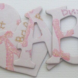 May include: Pink and gold wooden letters spelling out "ABC" with a pink heart that says "ballet" on it.