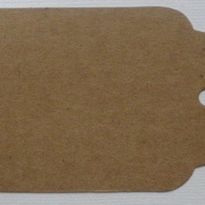 May include: A brown paper gift tag with a hole punched in the top right corner. The tag has a scalloped edge.