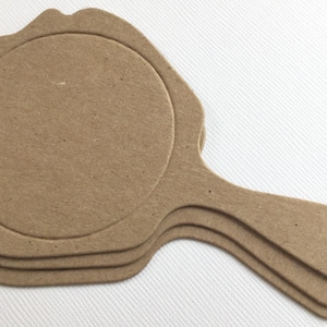 May include: Three brown cardboard craft blanks shaped like hand mirrors with a scalloped edge. The mirrors are stacked on top of each other.