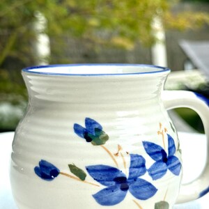 Peut inclure: Une tasse en céramique blanche avec un bord bleu et un motif floral bleu. Les fleurs sont stylisées et ont un schéma de couleurs bleu et jaune.