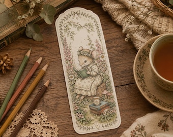 May include: A rectangular paper bookmark featuring a detailed illustration of a mouse wearing a floral crown and dress, sitting on a tree stump while reading a book. The scene includes surrounding flowers, a stack of books, and a small cup of tea.