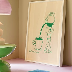 Puede incluir: Una impresi&oacute;n enmarcada con una ilustraci&oacute;n verde de una persona vertiendo caf&eacute; de una olla a una taza. El texto "fill your cup" est&aacute; debajo de la ilustraci&oacute;n.