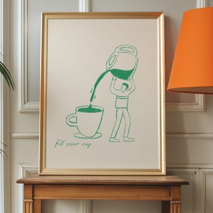 Puede incluir: Una ilustraci&oacute;n enmarcada de una persona vertiendo l&iacute;quido de una jarra grande en una taza. El texto "fill your cup" est&aacute; escrito debajo de la imagen. El marco es dorado y la imagen est&aacute; sobre un fondo beige claro.