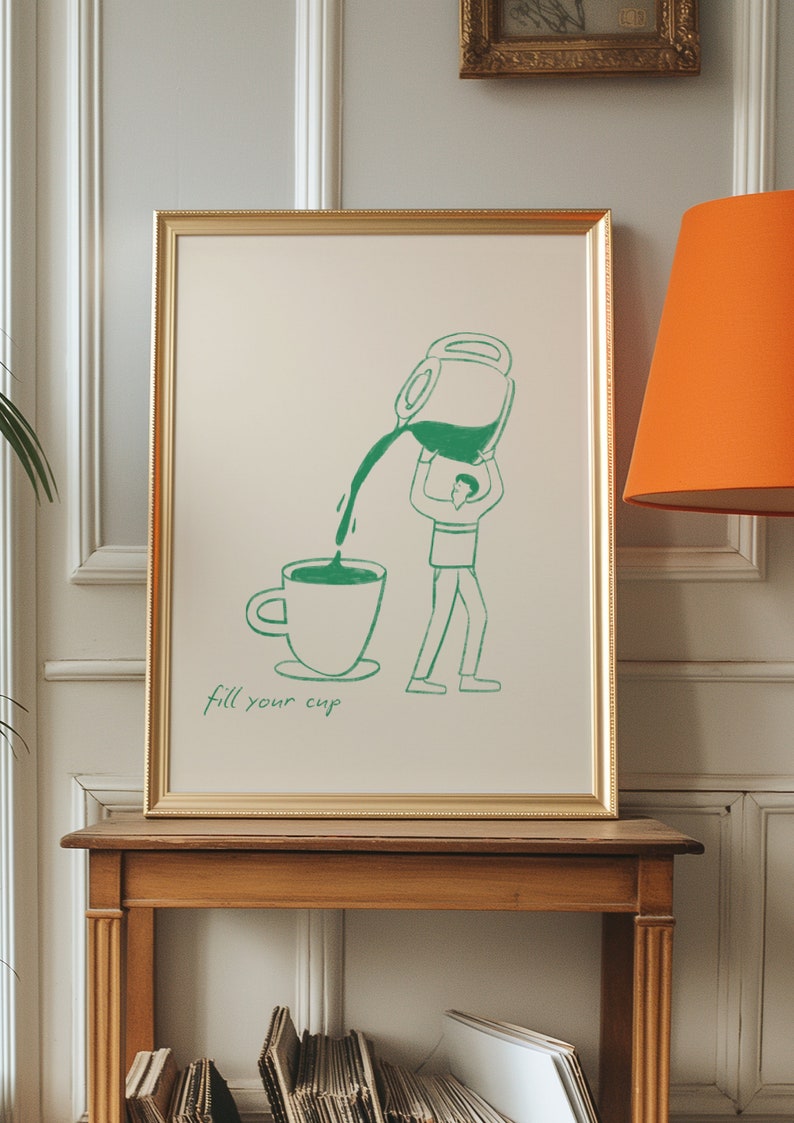 Puede incluir: Una ilustraci&oacute;n enmarcada de una persona vertiendo l&iacute;quido de una jarra grande en una taza. El texto "fill your cup" est&aacute; escrito debajo de la imagen. El marco es dorado y la imagen est&aacute; sobre un fondo beige claro.