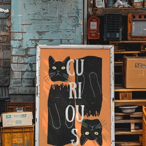 May include: A white framed poster with an orange background and two black cats. The cats are positioned to spell out the word "CURIOUS".