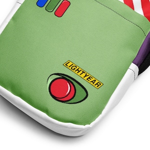 May include: A green fabric item with a white border, featuring a design inspired by the character Lightyear. The design includes the word "LIGHTYEAR" in yellow, a red and white eye-shaped graphic, and three rectangular shapes in blue, green, and red.