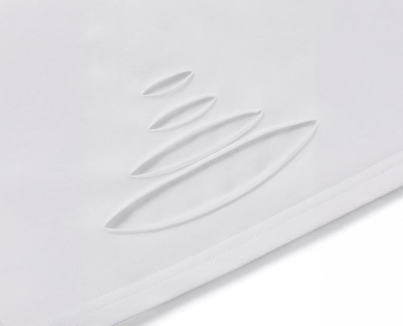 May include: Close-up of white fabric featuring several elongated, oval cut-outs. These are arranged diagonally, creating a textured effect. The fabric has a smooth, clean appearance, with a visible seam at the edge.
