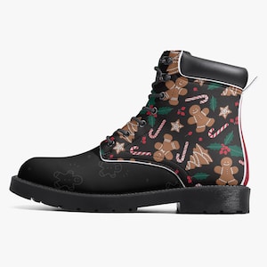 May include: Black combat boot featuring a festive Christmas pattern. The design includes gingerbread men, candy canes, stars, and holly leaves on a black background. The boot has a black sole, laces, and a white and red stripe detail.