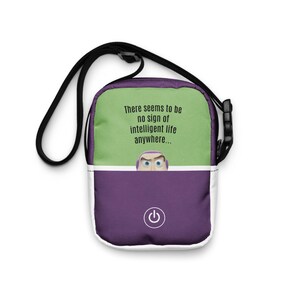 May include: A crossbody bag with a black strap, featuring a green top section with the text "There seems to be no sign of intelligent life anywhere..." and a purple bottom section with a power button graphic and a cartoon character.