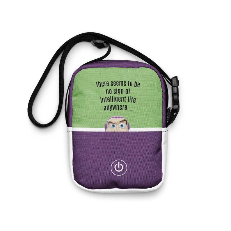 May include: A crossbody bag with a black strap, featuring a green top section with the text "There seems to be no sign of intelligent life anywhere..." and a purple bottom section with a power button graphic and a cartoon character.