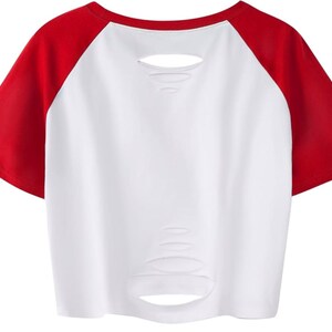 May include: White crop top with red raglan sleeves. The shirt features distressed detailing across the front. A casual style, suitable for everyday wear.