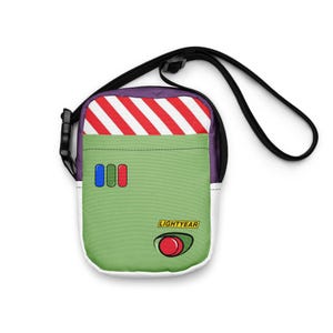 May include: A green and white crossbody bag with a black strap. The bag features a red and white striped top, three colored buttons, and the word "LIGHTYEAR" with a red button graphic. The bag is designed to resemble a character from a movie.