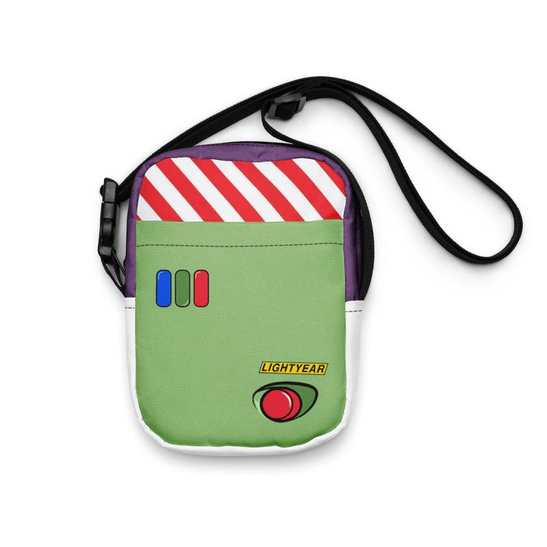 May include: A green and white crossbody bag with a black strap. The bag features a red and white striped top, three colored buttons, and the word "LIGHTYEAR" with a red button graphic. The bag is designed to resemble a character from a movie.