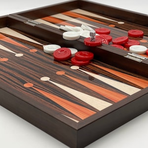 May include: A wooden backgammon board with a brown, orange and white striped design. The board is open and there are red and white playing pieces on the board. There are also two white dice on the board.
