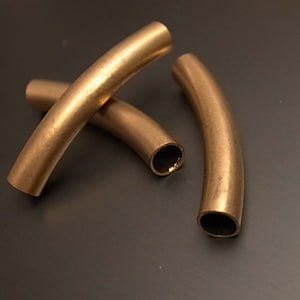 May include: Three gold-colored metal tubes, each bent into a gentle arc. The tubes are arranged in a criss-cross pattern.