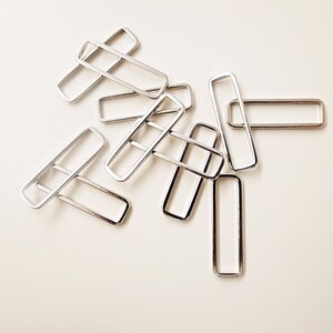 May include: A group of silver metal slider buckles, commonly used for straps and bags.