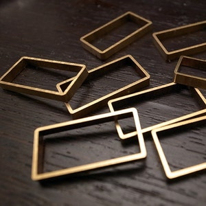 Puede incluir: Un conjunto de siete marcos rectangulares de metal dorado de diferentes tamaños, apilados y superpuestos sobre una superficie marrón oscura.