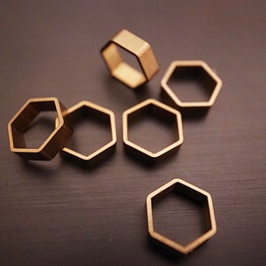 May include: Six gold-colored hexagonal rings, arranged in a cluster on a dark gray surface. The rings are all the same size and shape, and they are all made of a smooth, shiny metal.
