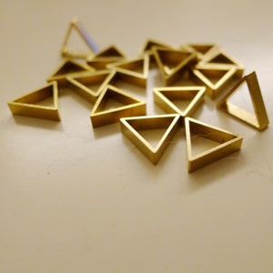 May include: A group of gold-colored metal triangles, arranged in a random pattern on a white surface.