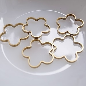 May include: Five gold-colored metal flower-shaped charms. The charms are all the same size and shape, and they are arranged in a pile on a white surface.